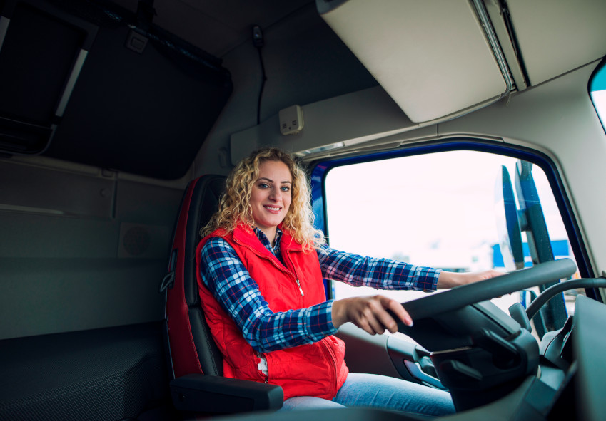 Portrait of trucker sitting in truck cabin with hands on steering wheel.